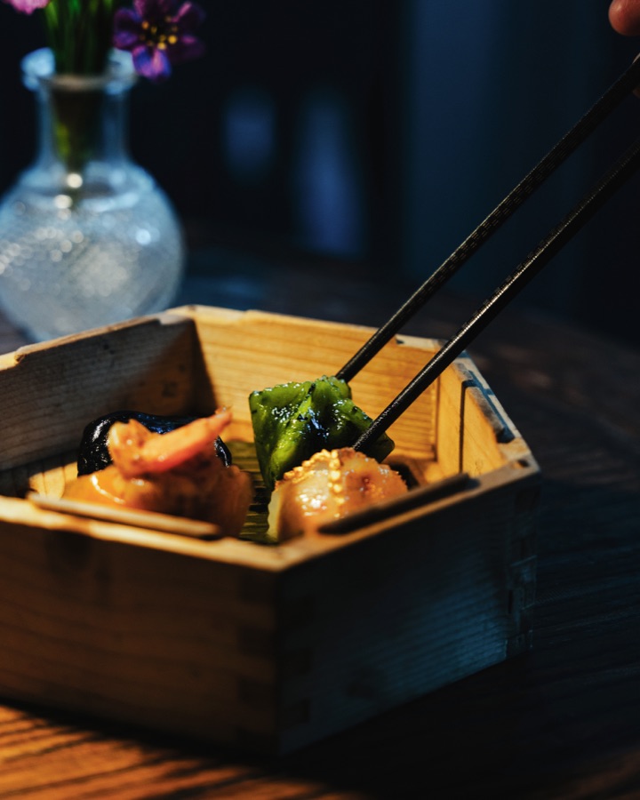 Chopsticks lifting a bite from a wooden box